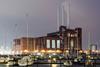 An old fashioned gas power station with boats in a harbour in front