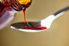 Red cough syrup being poured into a teaspoon