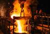 Two workers pouring molten metal from a large crucible into a mould