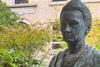 A bronze bust of Marie Curie in a courtyard garden