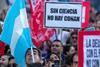 A large group of protesters. One is holding an Argentinian flag without the sun and one is holding a placard that says Sin Ciencia No Hay Conan (Without Science we have no Conan)