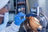 A gloved hand holds a pill up to the camera in a pharmaceutical lab