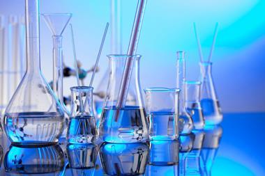 Various types of laboratory glassware, a thermometer and stirrers sitting on a surface with a blue background