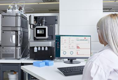 Scientist monitoring Waters Xevo TQ Absolute mass spectrometer and Acquity UPLC system with real-time data on a computer screen