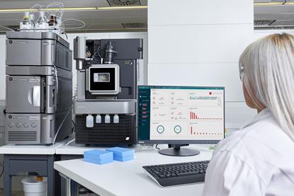 Scientist monitoring Waters Xevo TQ Absolute mass spectrometer and Acquity UPLC system with real-time data on a computer screen