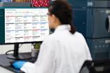 Scientist in lab monitoring multiple instruments using Waters System Monitoring software on a desktop screen