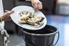 Someone scrapping their leftover fish from their plate into a bin