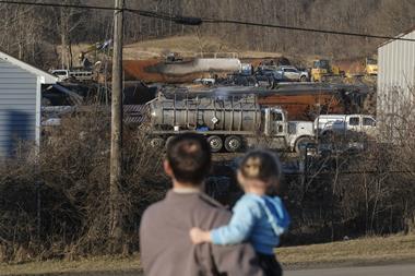 A father with his young daughter watch from a distance the clean up of a train derailment and fire